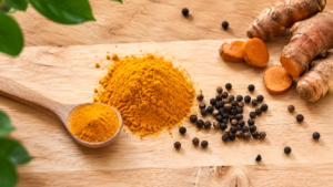 Poudre de curcuma et grains de poivre noir sur une planche en bois, avec une cuiller en bois
